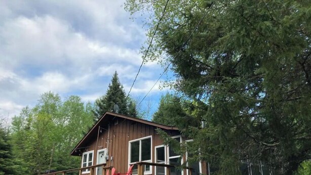 A wooden cabin with a deck, surrounded by trees.