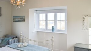 A bedroom with a bed, a dresser, a window with a view, and a chandelier. - 3 bedroom accommodation in Beadnell (Beadnell)