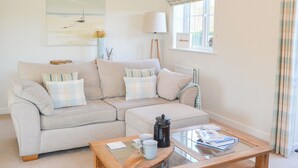 A living room with a beige sofa, a glass-top coffee table, and a painting of a sailboat on the wall. - 3 bedroom accommodation in Beadnell (Beadnell)