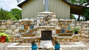 Un camino in pietra con una porta metallica, circondato da un muro di pietra con mensole che espongono oggetti decorativi.