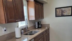 Una cocina con gabinetes de madera, lavavajillas de acero inoxidable, cafetera y un cuadro en la pared.