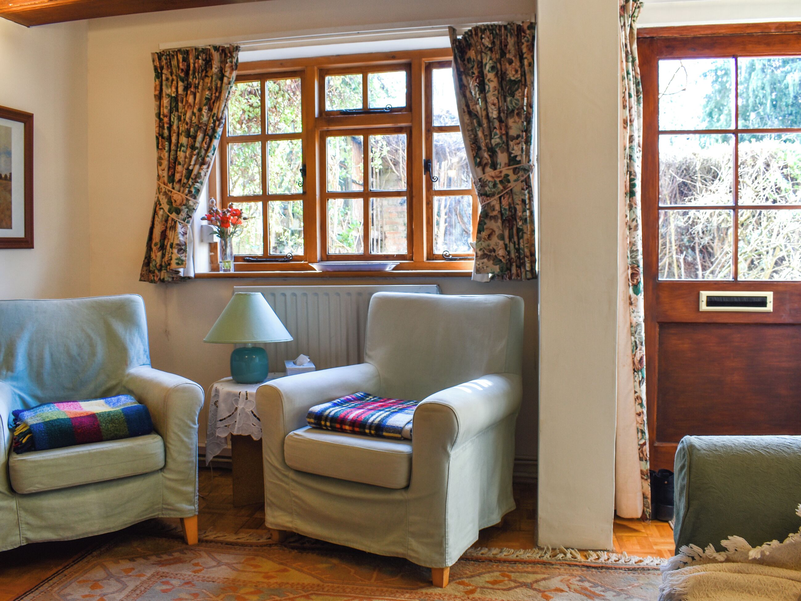 A cozy room with two armchairs, a small table with a lamp, and a window with floral curtains.