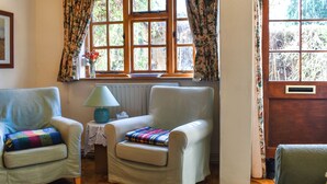 A cozy room with two armchairs, a small table with a lamp, and a window with floral curtains.