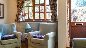 A cozy room with two armchairs, a small table with a lamp, and a window with floral curtains.