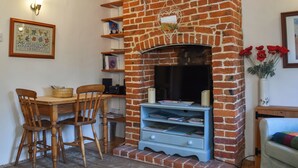 A living room with a brick fireplace, wooden chairs, a table, and a bookshelf.