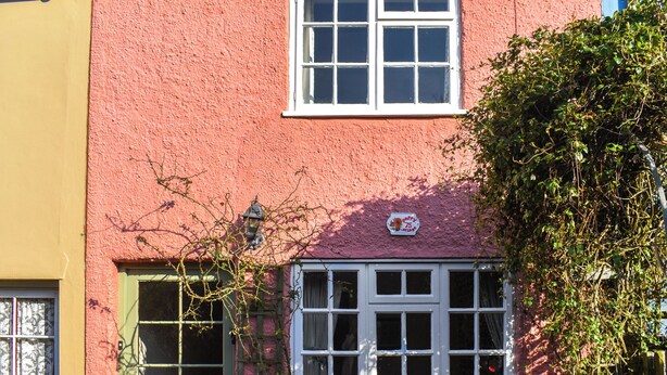 A pink building with a green door and a window with white shutters.