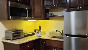 Une cuisine avec des meubles de rangement en bois foncé, un réfrigérateur en acier inoxydable, un four à micro-ondes et un four grille-pain.
