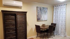 Un coin repas comprenant un buffet en bois, une table avec des chaises, un tableau accroché au mur et une fenêtre avec un rideau.