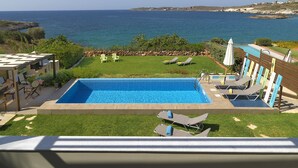 A pool area with a view of the sea, a grassy lawn, and lounge chairs.