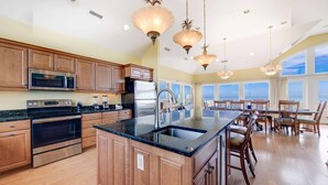 A spacious kitchen with wooden cabinets, stainless steel appliances, and a large island. - Oceanfront Home with Hot Tub, Pool, Putting Green, Elevator, and Game Room (Avon)