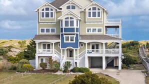 A multi-story house with a prominent front porch, a balcony on the second floor, and a garage. - Oceanfront Home with Hot Tub, Pool, Putting Green, Elevator, and Game Room (Avon)