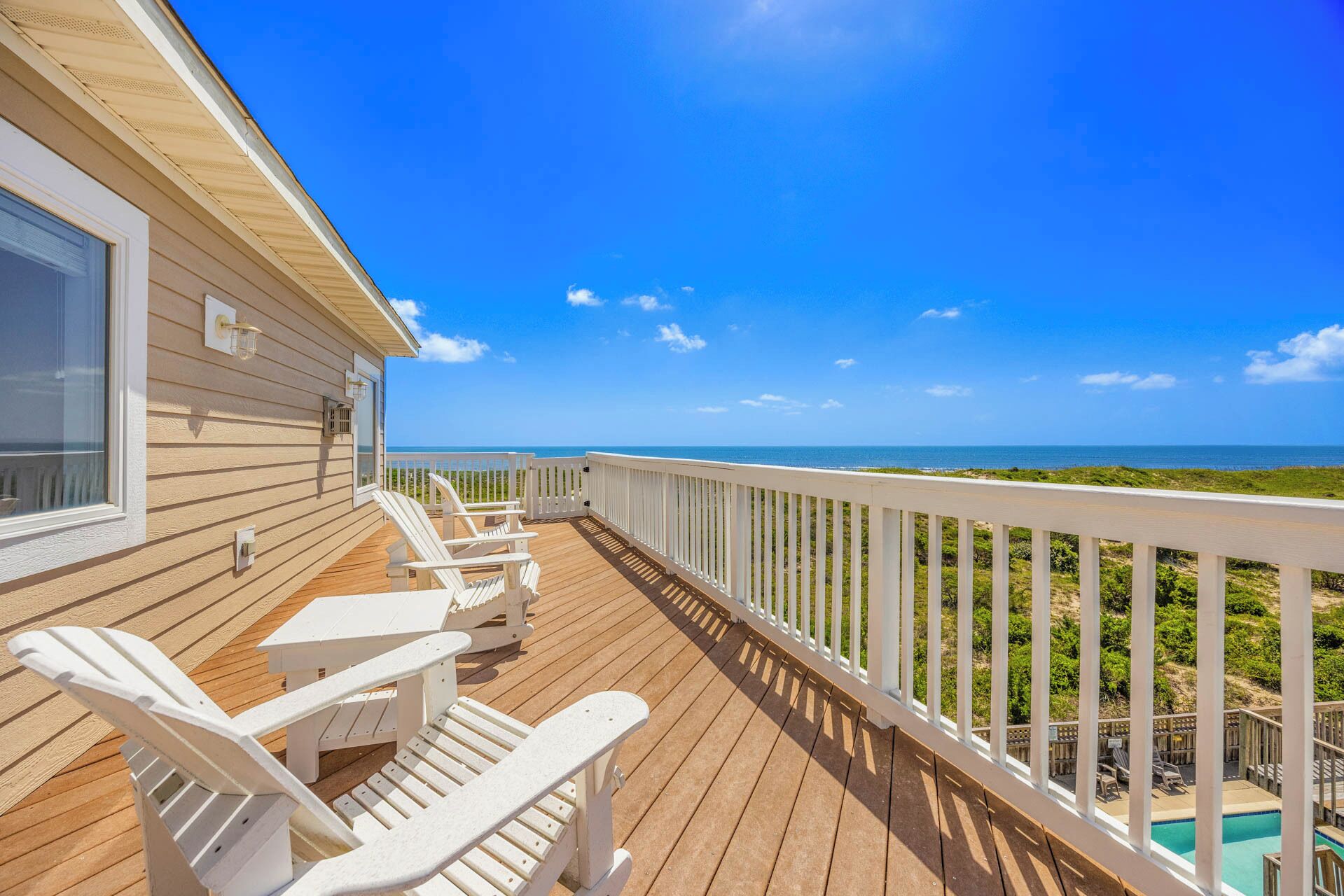 A wooden deck with white chairs and a view of the ocean.