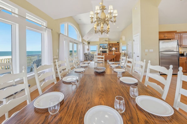 Uma sala de jantar com uma longa mesa de madeira posta para seis, cadeiras brancas e um candelabro.
