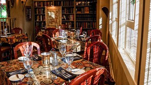 Un comedor con una mesa larga dispuesta para una comida, rodeado de estanterías llenas de libros.
