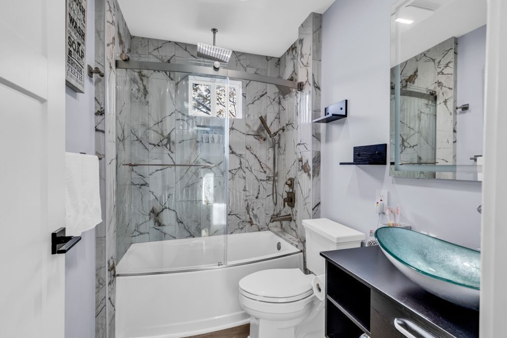 A modern bathroom with a glass-enclosed shower, a white toilet, and a glass vessel sink.