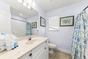 Une salle de bain avec un lavabo, des toilettes et un rideau de douche. On y trouve des serviettes et des articles de toilette sur le comptoir.