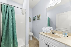 A bathroom with a shower, toilet, sink, and mirror. There are towels and toiletries on the sink counter.