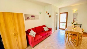 Una habitación con sofá rojo, armario de madera y una mesa de comedor con sillas.