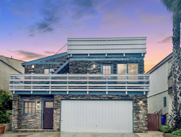 A two-story house with a stone facade, a white garage door, and a balcony with railings. - Beach Home-Rooftop Deck-Steps to Sand (Oxnard)