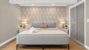 Une chambre moderne avec un grand lit, deux tables de chevet avec des lampes, un ventilateur de plafond et une porte coulissante.