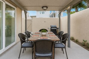An outdoor patio with a table set for four, surrounded by wicker chairs, a grill, and a potted plant. - Beach Home-Rooftop Deck-Steps to Sand (Oxnard)