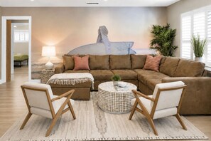 A living room with a large sectional sofa, two armchairs, a round coffee table, and a wall mural.
