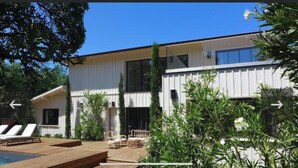 Un bâtiment moderne à deux étages doté d’un espace piscine, comprenant des chaises longues et une terrasse en bois.