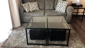 A living room with a grey sofa, patterned cushions, a glass coffee table, and a small side table with a lamp. - Lookout Mountain Lodge & Chalet with Views! (30 Day Min) (Golden)