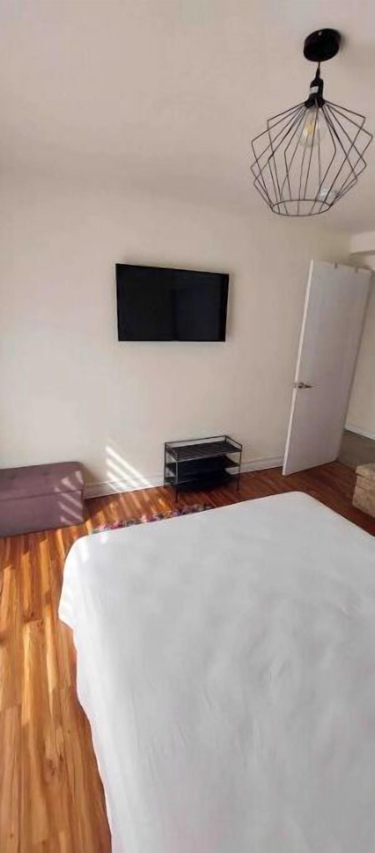A bedroom with a bed, a television mounted on the wall, a wardrobe, and a hanging light fixture.