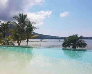 Una piscina cristalina con vistas a un cuerpo de agua tranquilo y montañas al fondo.