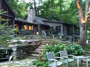 A rustic cabin with a stone chimney, wooden deck, and outdoor seating area.