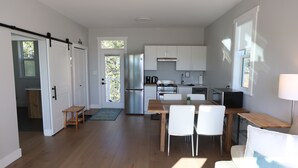 Una cocina moderna con electrodomésticos de acero inoxidable, un comedor con una mesa de madera y sillas blancas, y una puerta corrediza que da a otra habitación.