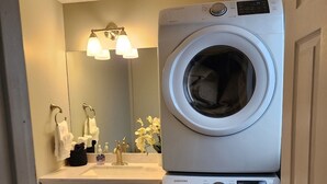 Une petite buanderie comprenant une machine à laver et un sèche-linge superposés, un meuble-lavabo avec un miroir et un petit évier.