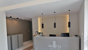 Una reception con un logo, una macchina per caffè e una pianta. Due lampade a sospensione nere sono posizionate sopra il bancone.