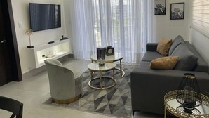 Un soggiorno moderno con un divano grigio, un tavolino rotondo, una poltrona bianca e una TV a parete.