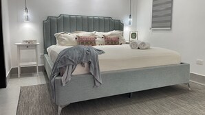 Una camera da letto moderna con un letto imbottito grigio, un comodino e una sveglia a parete.