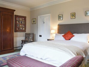 A neatly arranged bedroom with a large bed, a bedside table with a lamp, a chair, and a wooden wardrobe. - 4 bedroom accommodation in Kirkby Lonsdale (Kirkby Lonsdale)