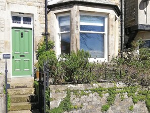 A stone building with a green door, a bay window, and a stone wall with ivy.