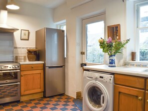 A kitchen with a refrigerator, oven, washing machine, and a window with a view.