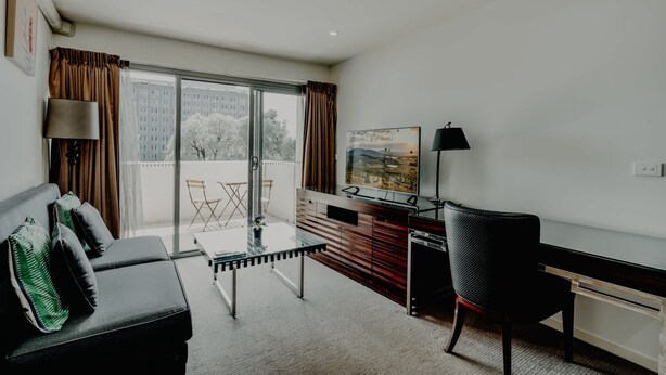 A modern hotel room with a sofa, a desk, a chair, and a large window offering a city view. - Urban 1-Bed Apartment in the Heart of the City (Braddon)