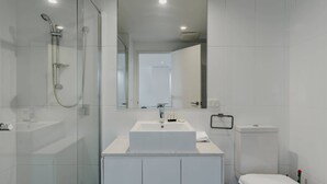 A modern bathroom with a glass shower enclosure, a white sink, and a toilet. - Urban 1-Bed Apartment in the Heart of the City (Braddon)