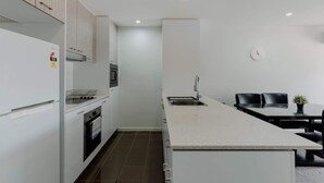 A modern kitchen with white cabinetry, a built-in oven, a microwave, and a stainless steel sink. - Urban 1-Bed Apartment in the Heart of the City (Braddon)