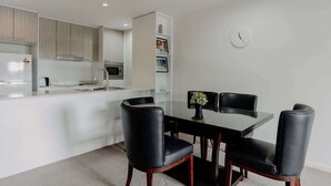 A modern kitchen with white cabinets, a microwave, and a sink. There is a dining area with a glass table and black chairs. - Urban 1-Bed Apartment in the Heart of the City (Braddon)