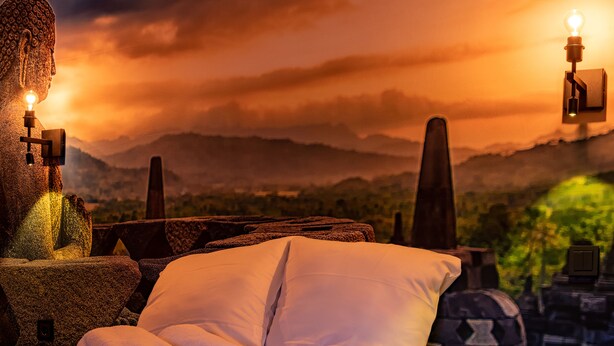 A bed with white linens and a towel, a stone sculpture, and a view of mountains at sunset. - Boutique Hotel Four (Geldrop)