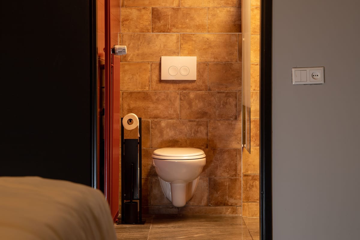 A bathroom with a toilet, a towel dispenser, and a wall-mounted electrical outlet.