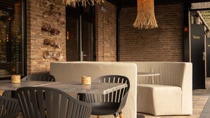An outdoor seating area with a brick wall, a woven light fixture, and a sign reading "Tuscany". - Boutique Hotel Four (Geldrop)