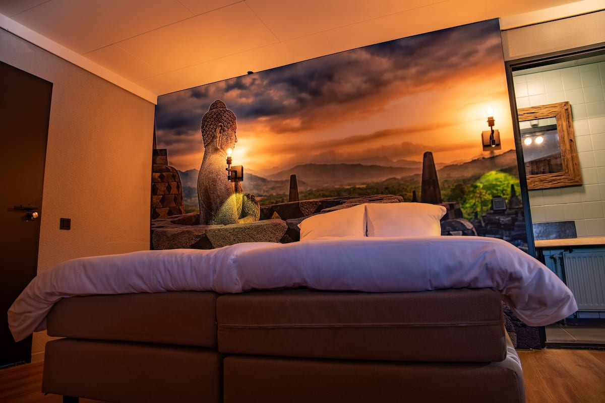 A bedroom with a large bed, a stone sculpture, and a sunset view.
