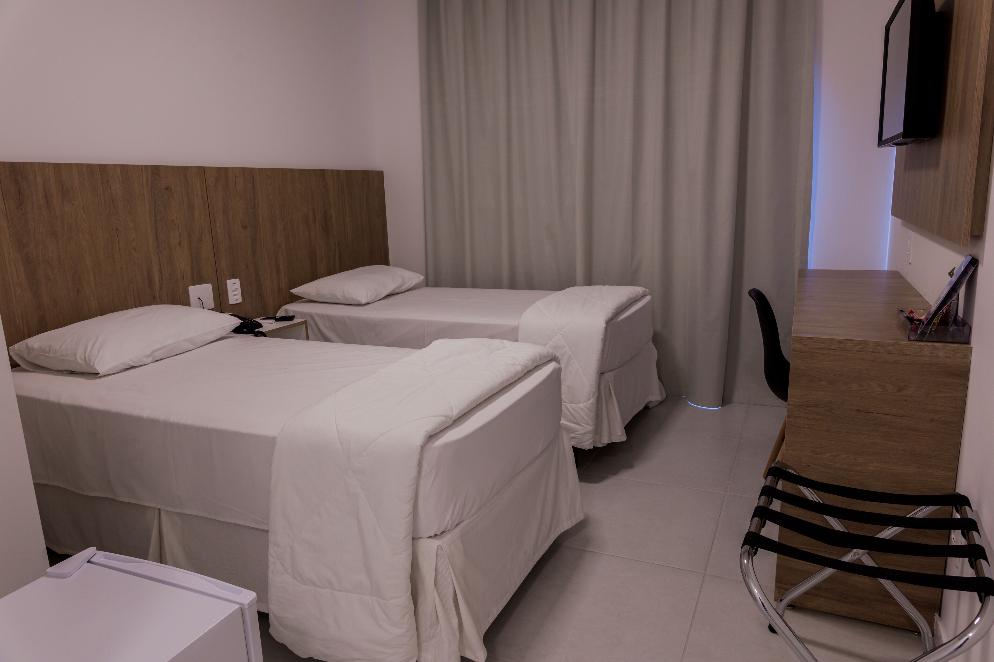 A hotel room with two beds, a desk, a chair, and a TV mounted on the wall.