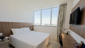 Habitación de hotel con una cama grande, un escritorio, una silla, un televisor y una ventana con vista a la ciudad.