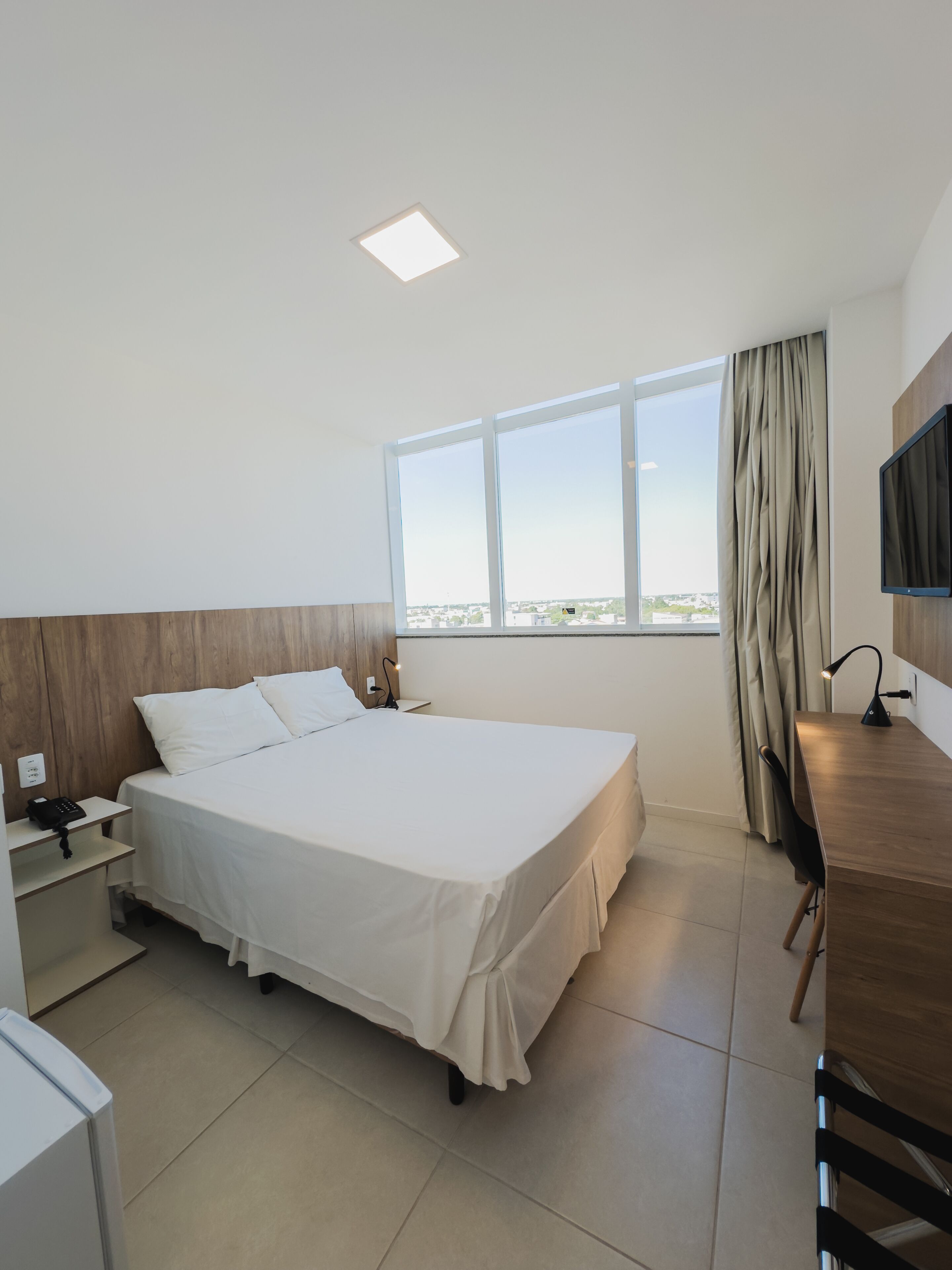 A hotel room with a bed, a desk, a chair, a TV, and a window with a view.